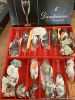 Photo showing organized Dampierre crystal stemware glasses in red trays, some individually wrapped in newspaper, with box labeling visible.