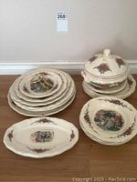 Photo showing stacked plates, bowls, and the soup tureen with lid on a wooden floor, Sarreguemines Obernai pattern visible with scenic and floral decoration.
