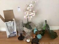 Crystal vases, artificial orchid, palm leaves, candle holders, and assorted small vases placed on floor near wall with box for Waterford crystal vase visible.