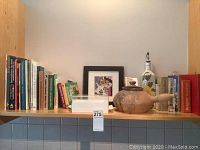 Bookshelf with assorted cookbooks, German-language books, a framed fruit picture, the Thomas clay oven, and a decorative bottle.