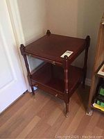 Front angle of wooden side table showing drawer and lower shelf with turned legs and casters.