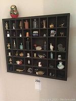 Full view of wall display with nesting doll on top, showing multiple compartments filled with miniatures.