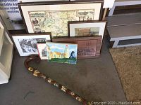 Photo of walking stick with multiple framed artworks and maps behind it, showing crest details on stick and map details.