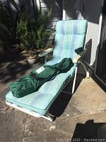 Front side view of the vintage white metal folding lounge chair with light blue striped cushion in sunlight on the patio.