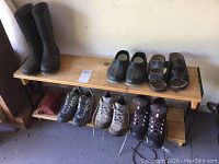 View of all footwear including tall black boots, two pairs of clogs, two pairs of hiking shoes, and wooden shoe rack with two levels