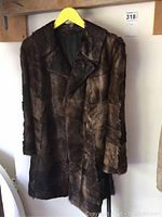 Front view of the brown fur coat hanging on a yellow hanger, shows overall length and collar.