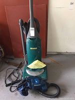 Front view of green Kenmore upright vacuum with attached hose and power cord. Blue Dirtbuster handheld vacuum placed at base.