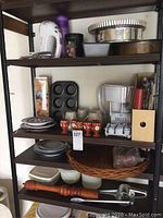 Full view of kitchen shelf with a white Westinghouse hand mixer, vintage egg cups, Brita pitcher, mugs, plates, muffin pan, knife block, and other kitchen items.