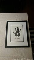 Framed print of a black handprint with Nelson Mandela's signature on white paper with matte border.