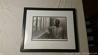 Front view of framed black and white photograph depicting Nelson Mandela looking through prison bars.