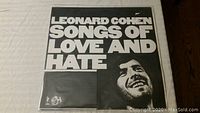 Front cover of Leonard Cohen vinyl album Songs of Love and Hate showing black and white design with Cohen's smiling face and bold white text.