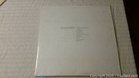 Front of James Taylor vinyl album cover showing minimalist white design with artist name and song list.