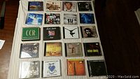 Top-down photo of 20 CDs arranged in 4 rows showing album cover art including Creedence Clearwater Revival and Miles Davis.