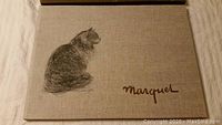 Beige hardcover book with textured cloth cover showing a detailed pencil sketch of a cat and 'Marquet' signature.