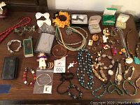 Overview of assorted costume jewelry and watches on a wooden surface including multiple necklaces, pins, bracelets, and rings.