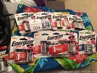 Multiple unopened Energizer batteries including AAA, AA, and 9V on colorful fabric background.