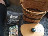 Longaberger basket, fabric liner in sealed bag, wooden lid with green knob on carpet floor