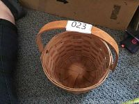 View from the side and top angle of the small round basket with handle, showing basket height, handle attachment, and overall condition.