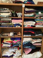 Full view of a wooden bookcase shelf filled with folded sewing fabric, spools of thread, and sewing tools.