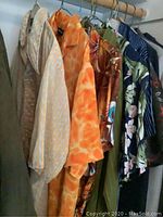View of multiple vintage styled men's shirts hanging closely together, showing variety of patterns including beige, orange, brown floral, green, and blue floral designs.