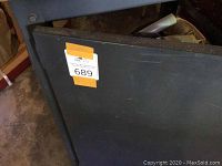 Photo of the side of the metal storage bench showing its black metal side surface with auction tag