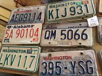 Photo showing six license plates from Washington, Alabama, Illinois states, including date stickers from 1984 and 1985.