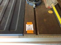 Close-up photo of the adjustable fence rail, showing measuring rulers and the saw table surface with wear.