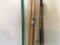 Photo showing a side view of the tools leaning against a wall including the shovel, post hole digger, a green handled tool and a spud bar.