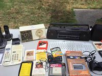 Photo showing overview of electronics on table including phones, radio clock, cassette player, keyboard, and accessories.