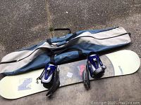 Photo showing the full snowboard with attached purple bindings and the gray-blue Lamar carrying bag.