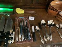 Overview of knives, wooden tray, flatware and silicone brush on wooden surface