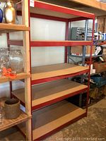 Full view of red metal utility shelf with four particle board shelves in a garage/storage setting.