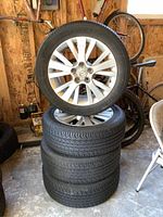 Four stacked tires with one tire mounted to Mazda alloy wheel with visible spokes and center cap.