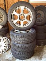 Four Bridgestone winter tires stacked with one showing mounted alloy rim and multiple spoke design.