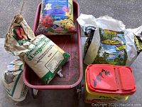 Overview of red Radio Flyer wagon containing multiple bags of gardening supplies including fertilizers and soil amendments, along with a flower food container.