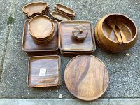 Set of wooden bowls, plates, serving utensils, and dishes laid out on ground