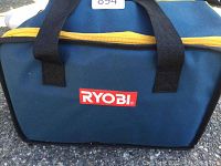 Front view of blue Ryobi canvas carry bag with yellow zipper and black straps on asphalt surface.