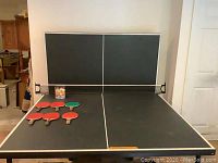 Full ping-pong table with net, displaying paddles and ping-pong balls arranged on the table surface.
