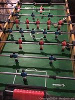 Close-up view of foosball player figures and playing field in green with white markings. Two teams, red and blue, on chrome rods.