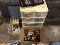 Photo showing plastic drawers with sewing supplies, cardboard box filled with multi-colored sewing thread spools, and a plastic container with craft items.