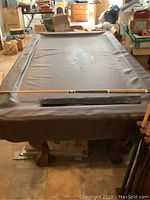 Full view of pool table covered with fitted cover, single cue laid across