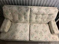 Top-down view of floral pattern love seat with cushioned armrests, tufted backrest, and subtle wear marks on fabric.