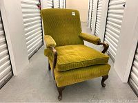 Front view showing green corduroy upholstered armchair with cushion and exposed wooden armrests and legs.