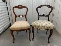 Two antique dining chairs side by side showing carved wood frames and upholstered seats with floral patterns.