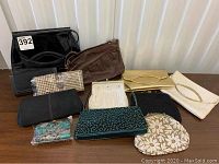 Overview of various evening bags, clutches and handbags arranged on a table including fabric, leather, and beaded bags.
