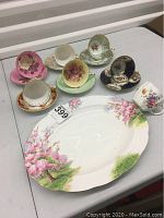 Overhead view of six tea cup-and-saucer sets, one single cup, and serving platter