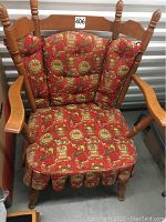 Front view of the wooden armchair with red patterned cushions showing overall design and visible scratches.