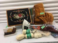 Wide view showing wooden footstool with needlepoint floral design, balls of wool yarn, knitting needles, tartan handkerchief, and Black & Decker iron.