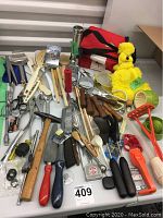 Photo showing a collection of vintage kitchen utensils including wooden spoons, knives, graters, scissors, mallet, and a yellow plush tea cozy.