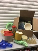 Box and assortment of plastic containers, kitchen accessories including green ice trays and funnels, and small kitchen items.